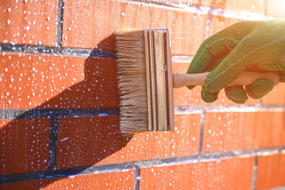 Worker applying waterproof coating to a brick masonry wall to prevent moisture infiltration.